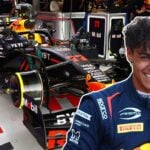 En ung förare i Prema Racing-overall med ett stort leende står framför en Red Bull Formel 1-bil i ett F1-garage. Bilen och teamets utrustning syns tydligt i bakgrunden, med logotyper från sponsorer som Oracle och Mobil.
