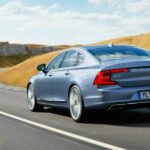 Ljusblå Volvo S90 snett bakifrån på landsväg.