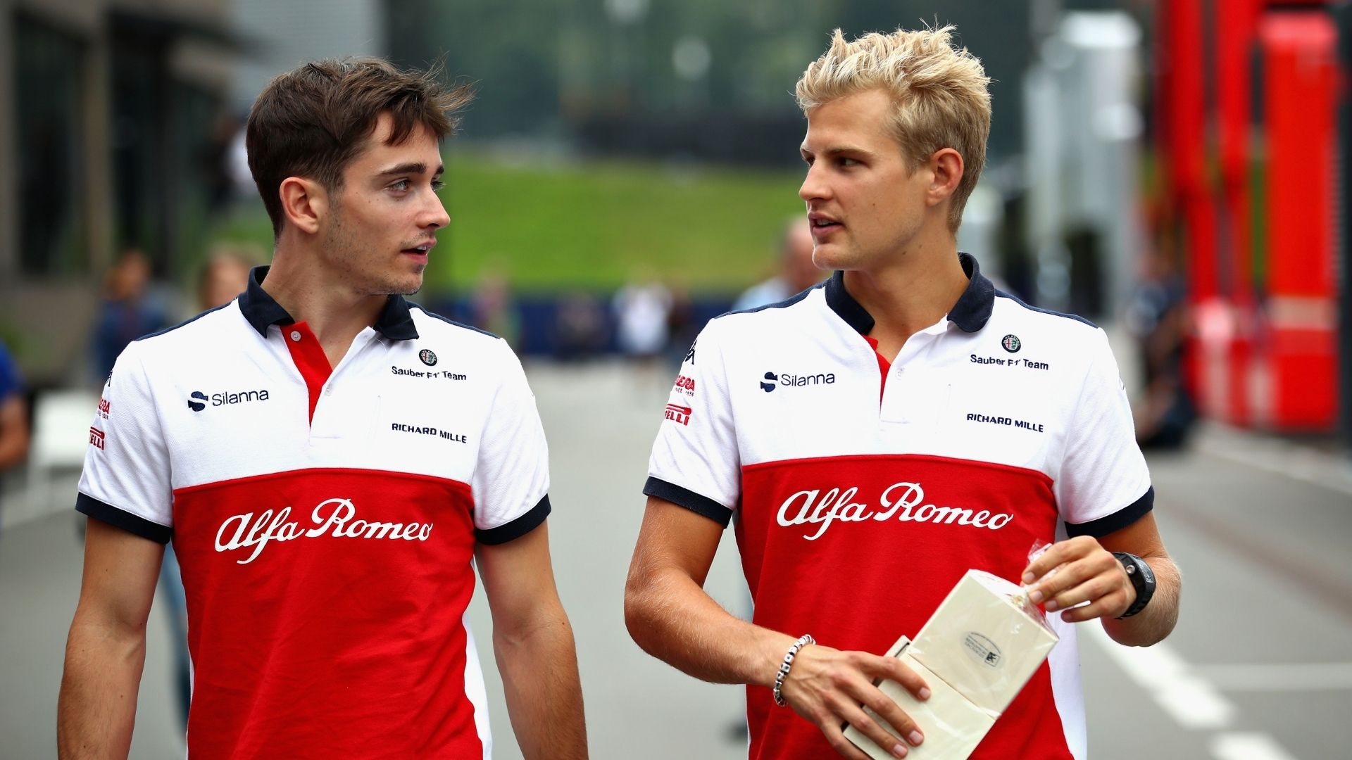 Charles Leclerc och Marcus Ericsson i Sauber-teamkläder från F1-säsongen 2018, promenerar tillsammans i depån och samtalar inför en tävling.