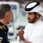 En man i Red Bull-kläder samtalar med en annan man klädd i en traditionell vit arabisk dräkt, som pekar med fingret i en intensiv diskussion i en Formel 1-depåmiljö.