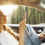 Ung kvinna som kollar på sin mobiltelefon samtidigt som hon kör utan säkerhetsbälte.