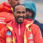 Lewis Hamilton ler stort i sin nya Ferrari-uniform under en regnig dag på banan, omgiven av teammedlemmar.