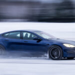 Blå Tesla Model S Plaid kör på snöbelaggd väg.