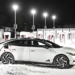 Vit Volkswagen ID.7 laddar vid Tesla Supercharger i vinterväder.