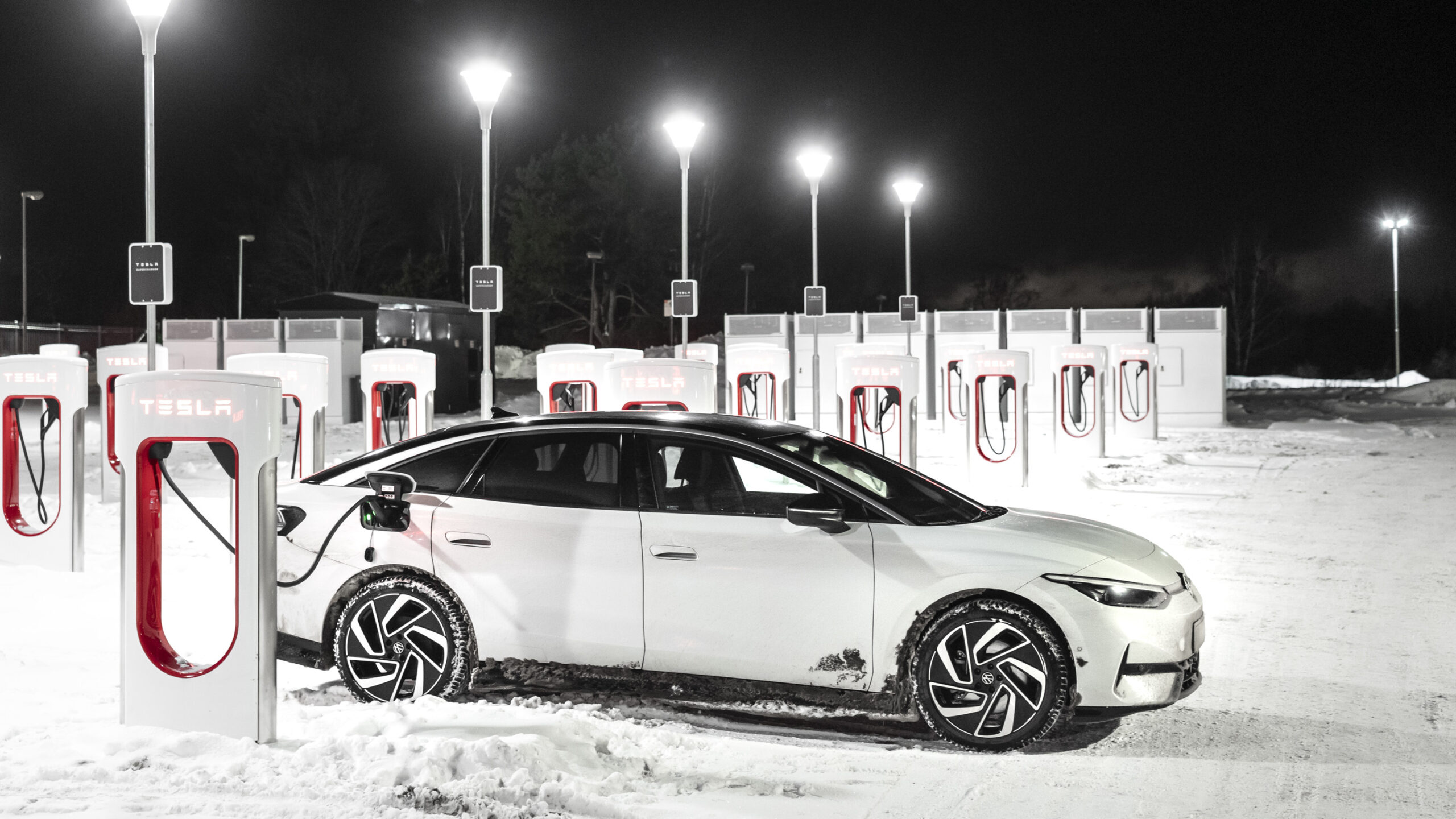 Vit Volkswagen ID.7 laddar vid Tesla Supercharger i vinterväder.