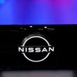 Närbild av Nissans logotyp visad på en mobilskärm, med en futuristisk bakgrund i blått och lila.