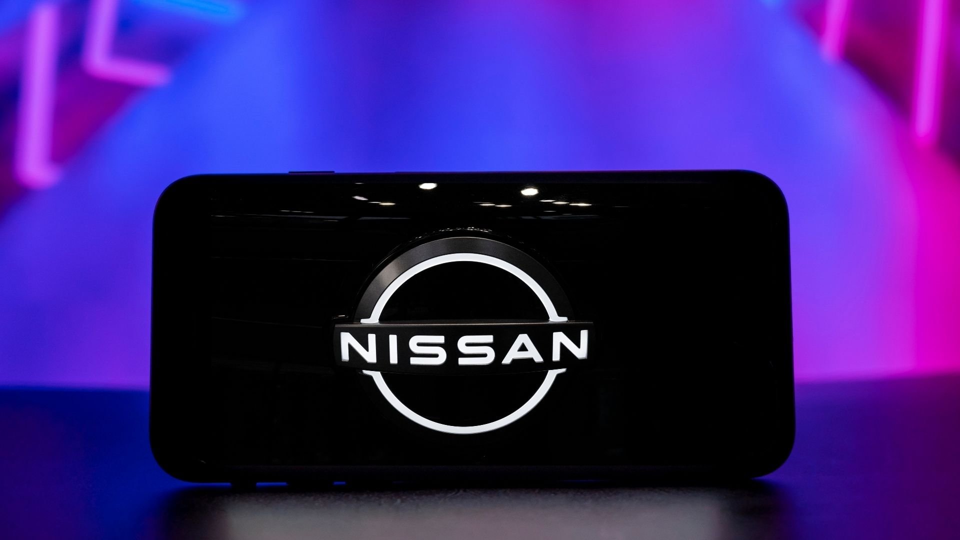Närbild av Nissans logotyp visad på en mobilskärm, med en futuristisk bakgrund i blått och lila.