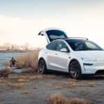 Nya Tesla Model Y i vitt står med bagageluckan öppen och två människor paddlar i vattnet bakom.