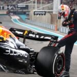 En Red Bull RB20 står stilla på banan med en förare i Red Bulls tävlingsoverall som frustrerat sparkar på bilen efter tekniska problem under ett lopp.