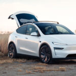 Nya Tesla Model Y i vitt står på strand med bakluckan öppen.