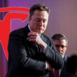 Elon Musk står på scen under en presentation. Tesla-logotypen syns som ett montage i bakgrunden. Diskussioner pågår kring hans ledarskap och varumärkets framtid.