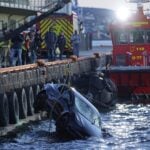 En Tesla lyfts upp ur Oslofjorden av räddningstjänsten, omgiven av brandmän och en räddningsbåt. Bilen är delvis nedsänkt i vattnet.