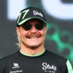 Valtteri Bottas ler stort i sin teamkeps och solglasögon under ett event, iförd sin racingoverall från Stake F1 Team.