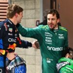 Max Verstappen i Red Bull-ställ och Fernando Alonso i Aston Martin-kläder står tillsammans och ler medan de håller sina hjälmar.